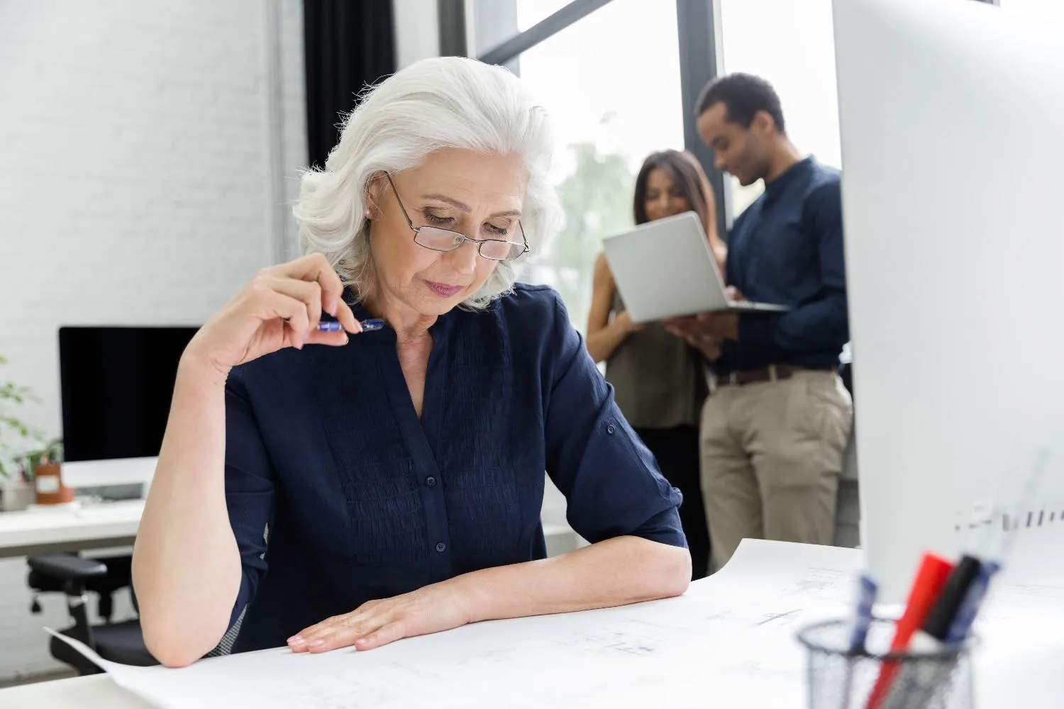 An older woman going over papers at a desk with a pen in hand